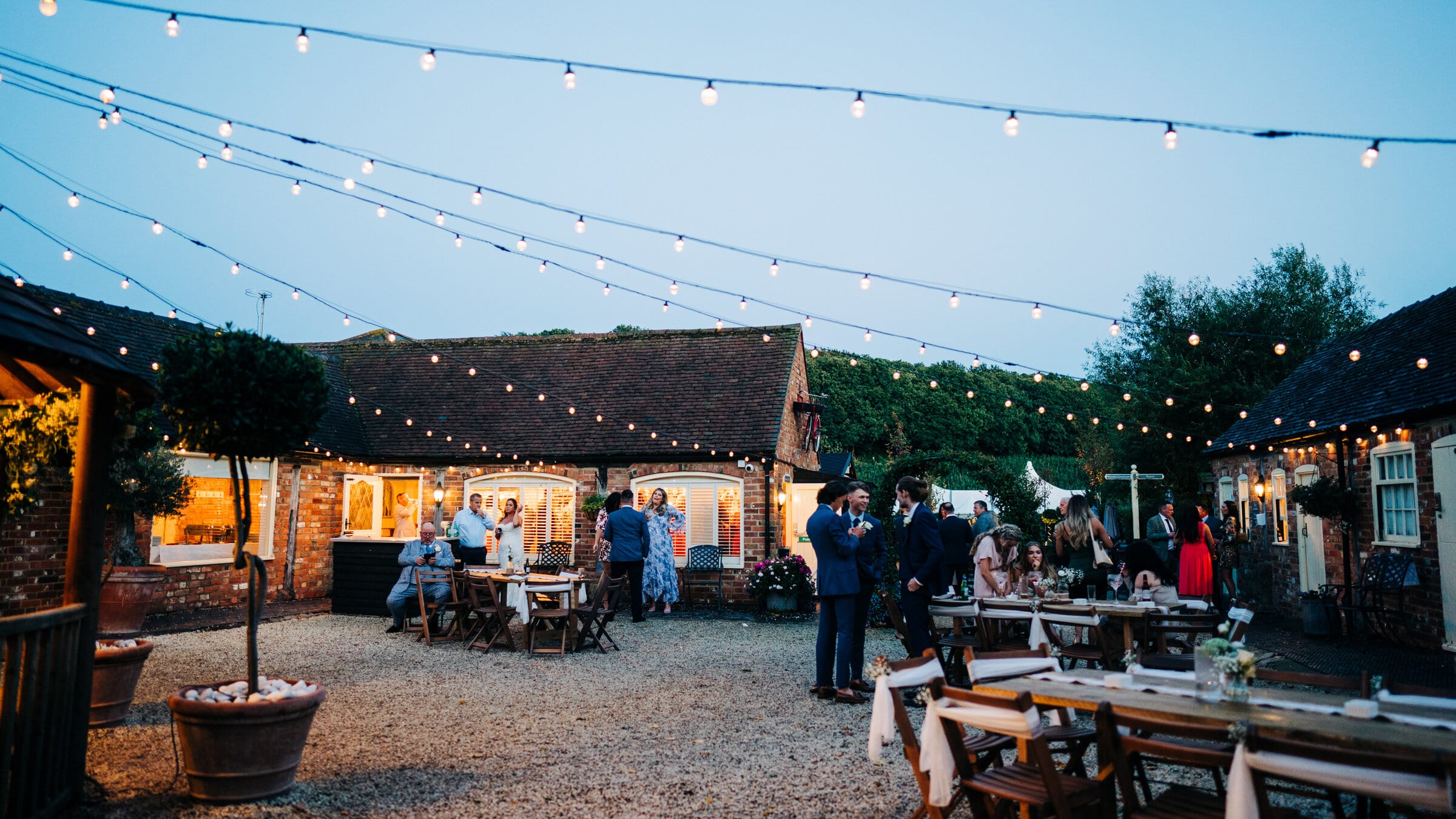 The CourtYard at The BarnYard glowing at dusk for an evening party, with festoon lights and guests