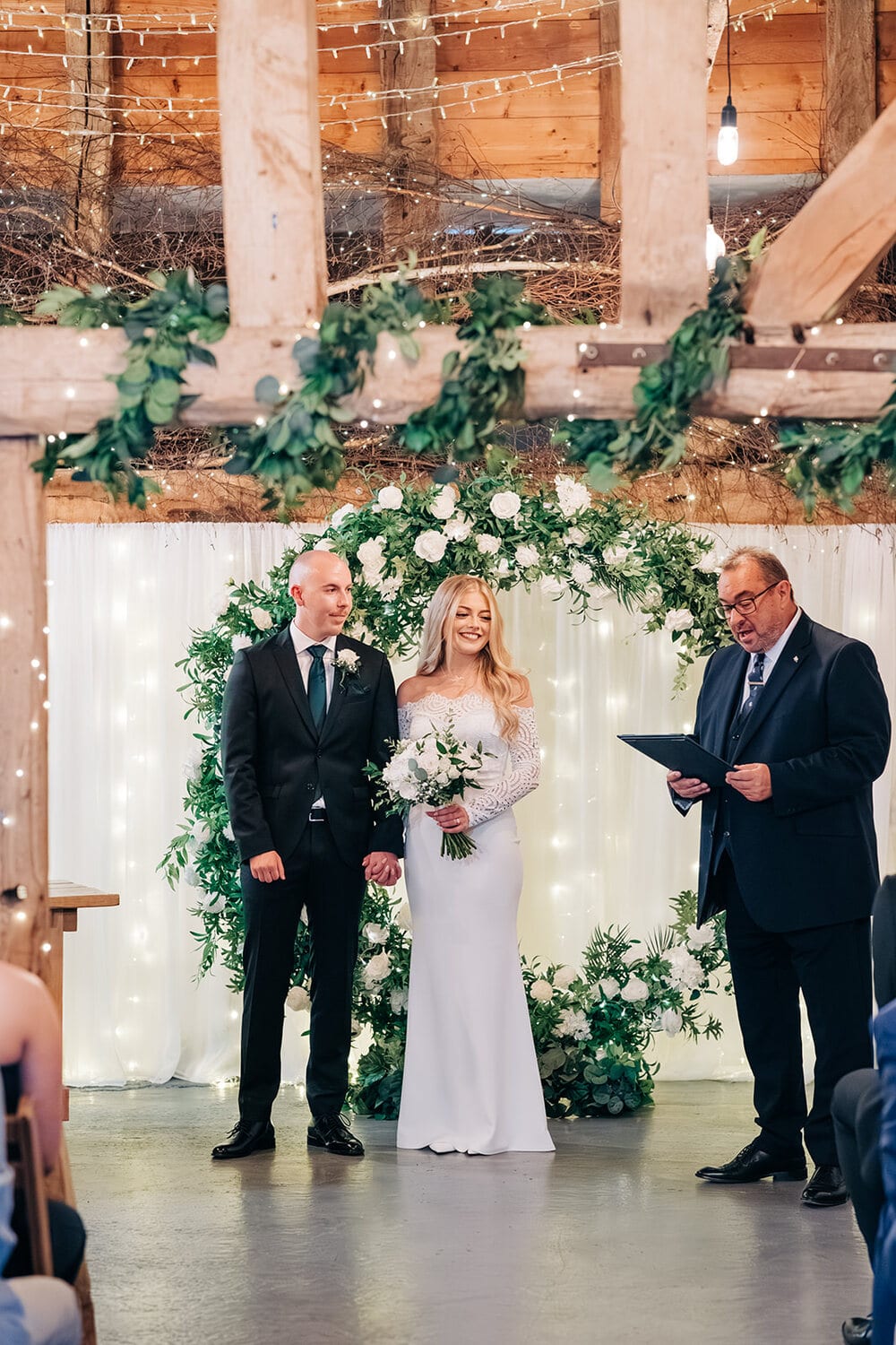 A couple at a foliage and fairy-light arch in the Apple Barn