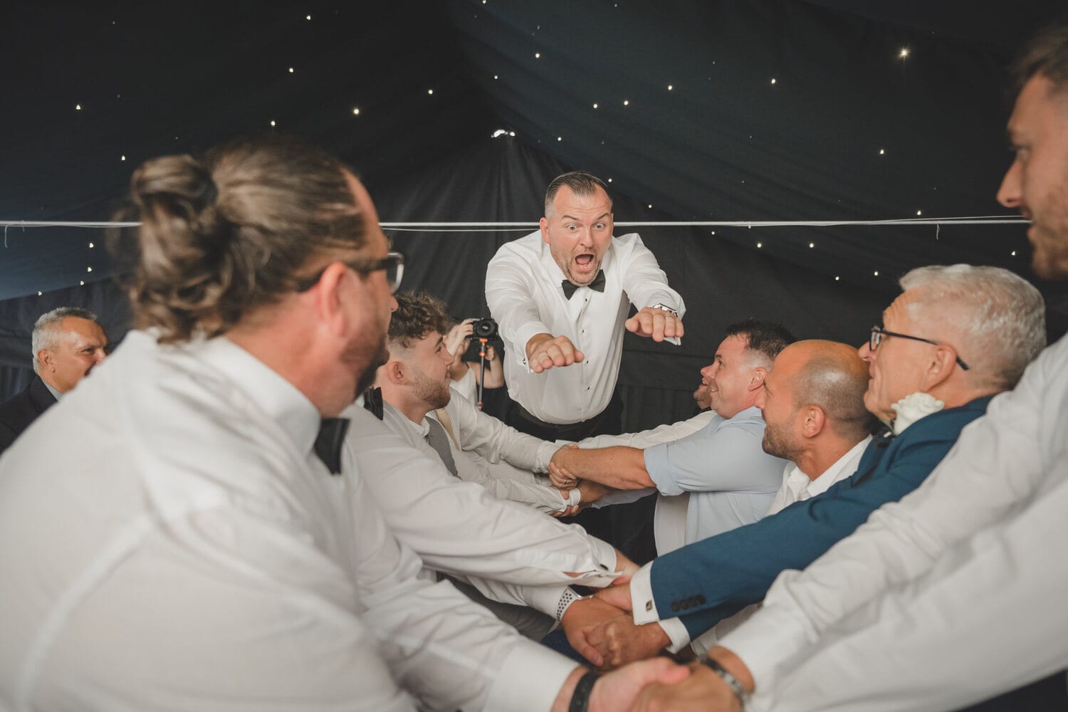 A groom lifted by guests on the dancefloor
