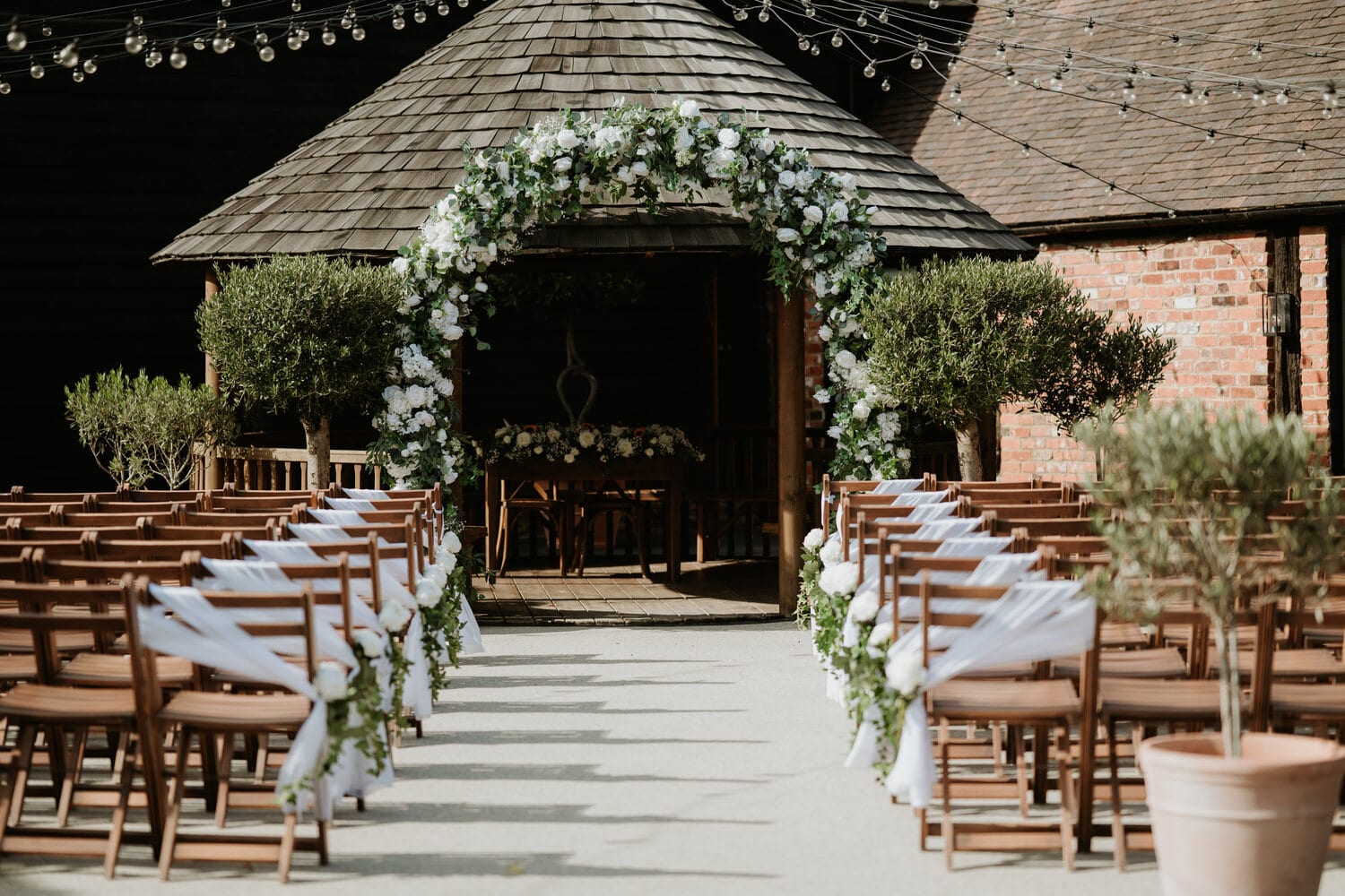 Rows of chairs and a foliage arch set in the courtyard by the Apple Barn