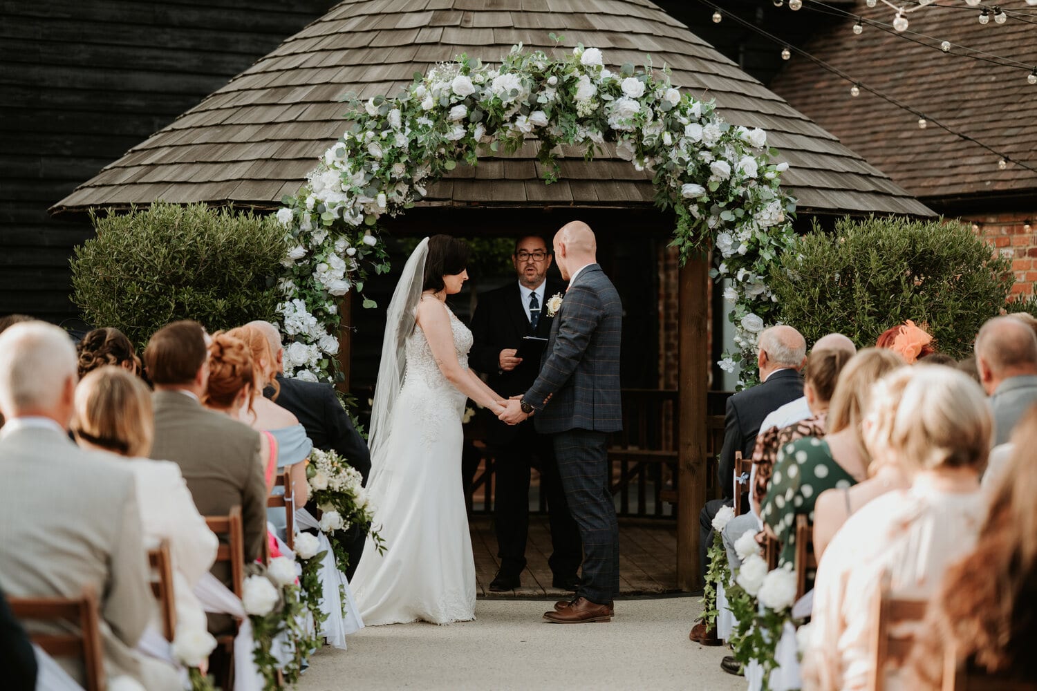 A couple exchange vows beneath a greenery arch in the courtyard