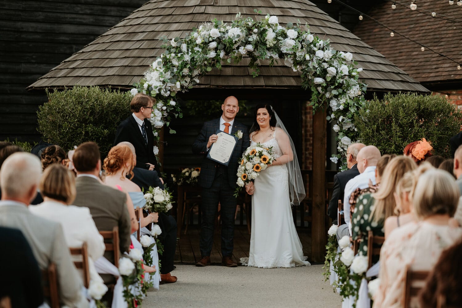 A couple at a foliage arch in the courtyard with guests