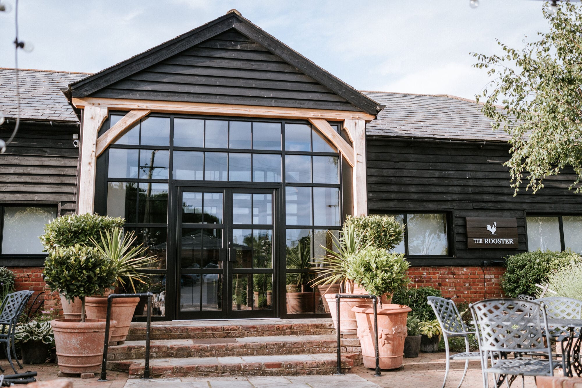 The Rooster restaurant at The BarnYard in Kent, a black timber barn with a glass A-frame entrance and terrace seating