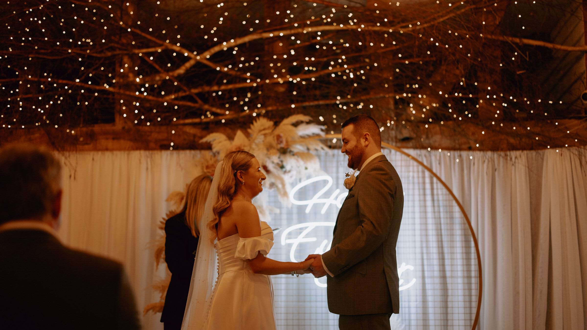 A couple at their fairy-lit wedding ceremony at The BarnYard in Kent